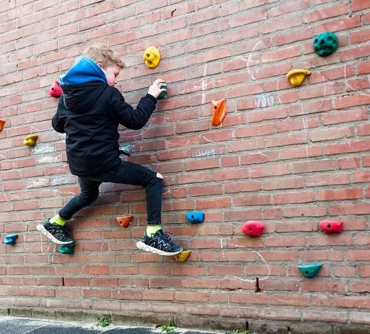 Jongen klimt op klimstenen tegen de schoolmuur