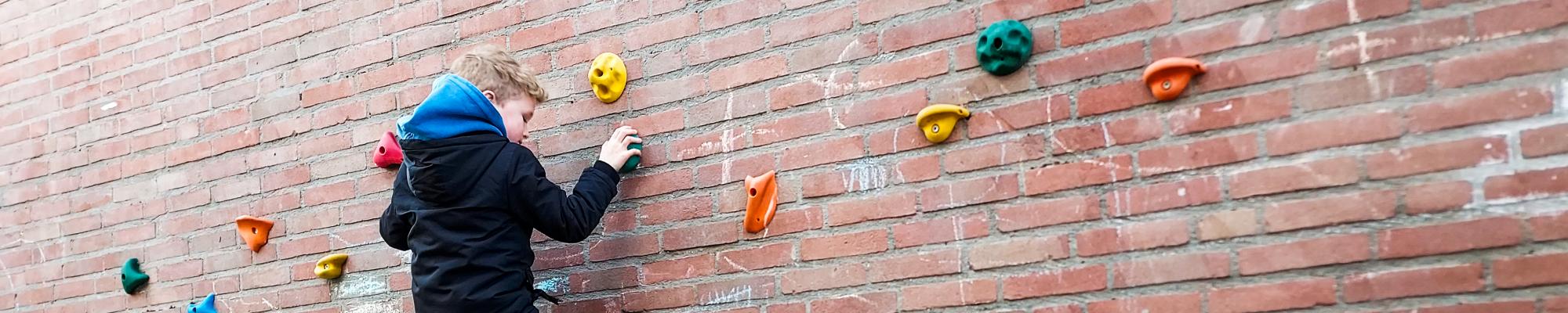 Jongen klimt op klimstenen tegen de schoolmuur